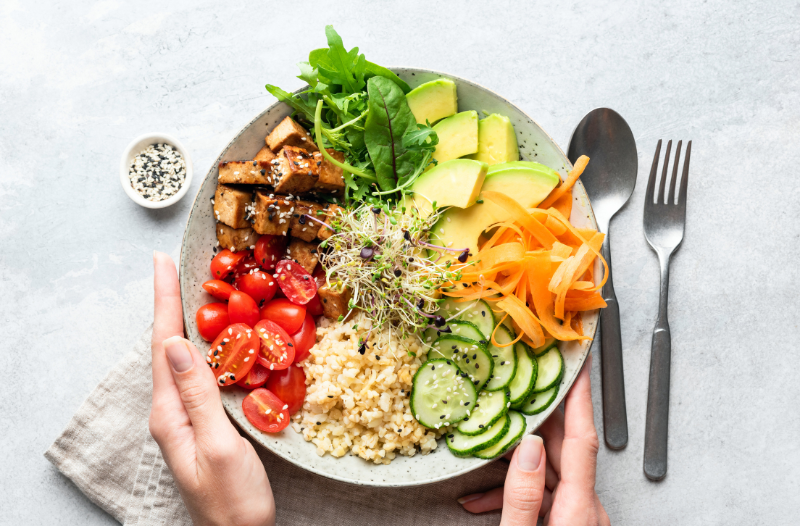 Balanced meal including tofu, spinach, avocado, shaved carrots, cucumbers, rice, tomatoes, sprouts and a side of sesame seeds. 