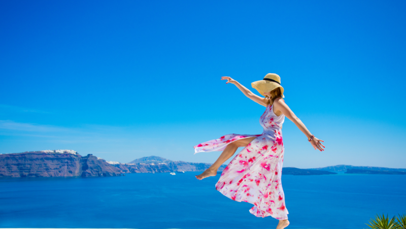 woman living carefree wearing a pink and white dress and floppy hat. background in the ocean with mountains