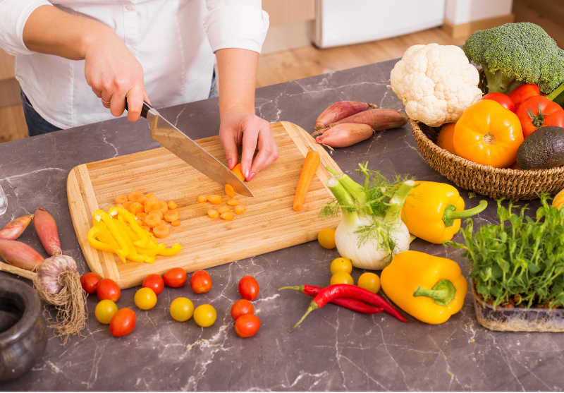 Woman chopping carrots and peppers, basket full of vegetables in the background