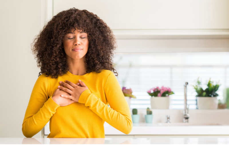 woman with hands over heart in gratitude. kitchen sink n the background with plants