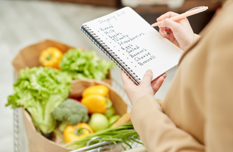 Woman writing grocery list with grocery bag filled with vegetables