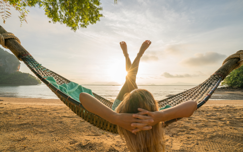 woman with blond hair sitting on the beach in a hammock