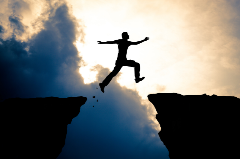 man jumping from one cliff to another with his hands in the air